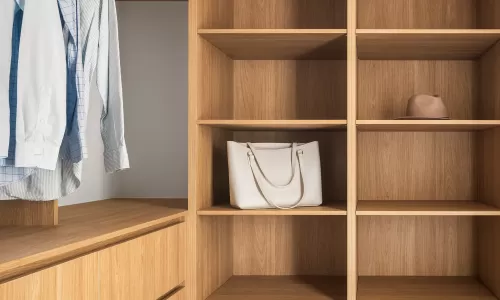 Walk-in closet with wooden shelves, hanging shirts, a white handbag, and a hat on the shelves