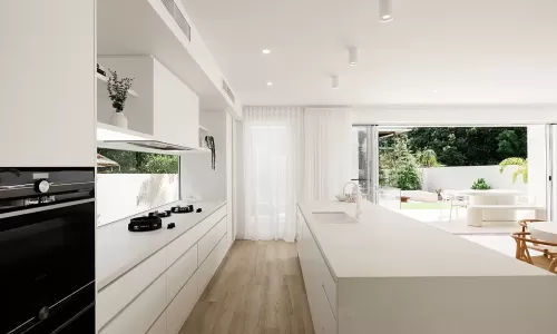 Modern kitchen with white cabinets, countertops and appliances, light wood flooring, and a view of an outdoor patio through sliding glass doors with sheer curtains