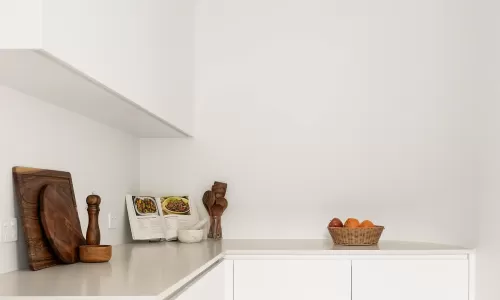 Minimalist white kitchen nook with wooden cutting boards, utensils, a cookbook, and a fruit basket