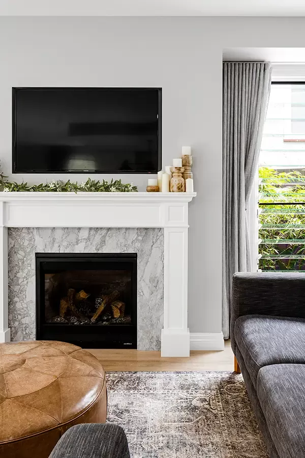 A modern living room with a flat-screen TV mounted above a marble fireplace, surrounded by decorative candles and greenery