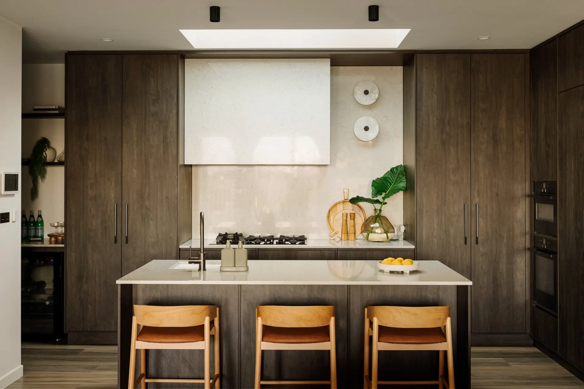 Modern kitchen with dark timber cabinetry, white island and wooden bar stools under a skylight