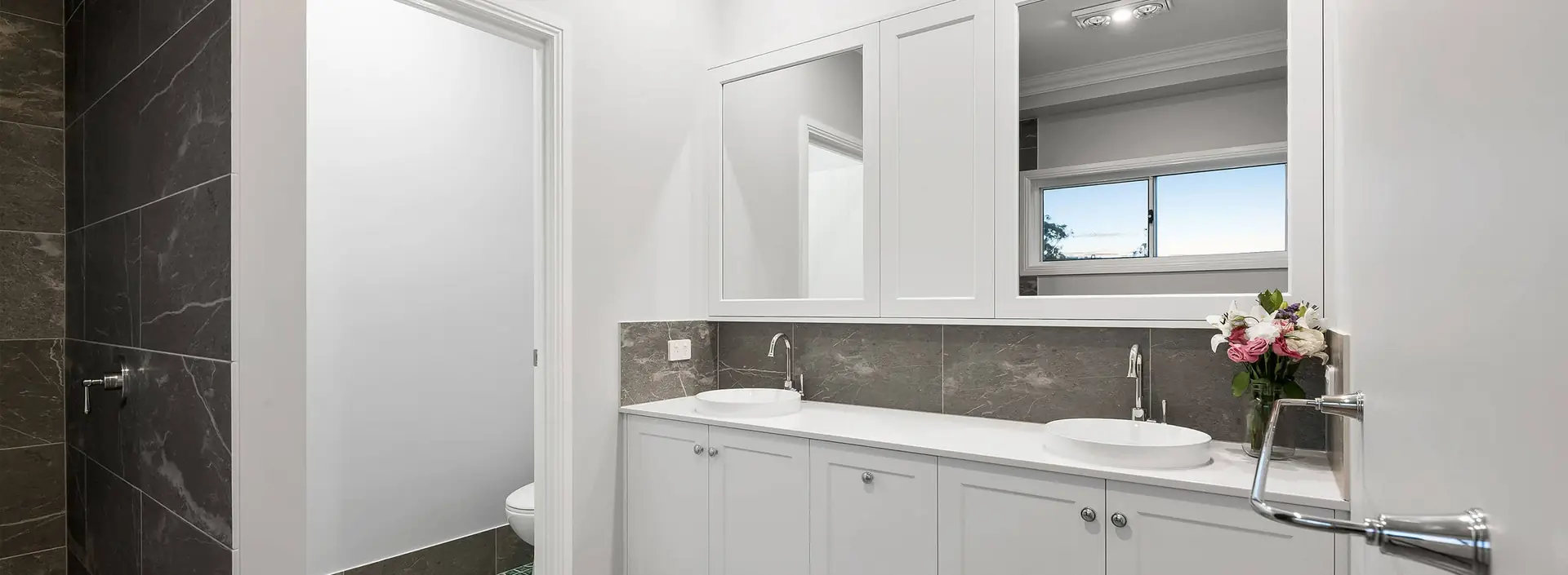 White bathroom vanity with vessel sinks, chrome taps and marble-tile splashback by Weston Kitchens and Bathrooms