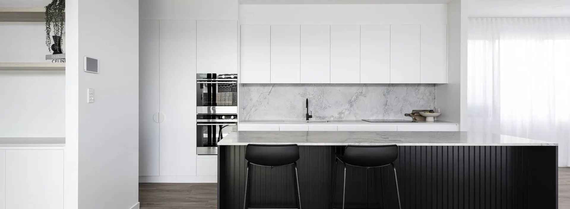 Black fluted kitchen island with marble benchtop, white cabinetry and black bar stools by Weston Kitchens
