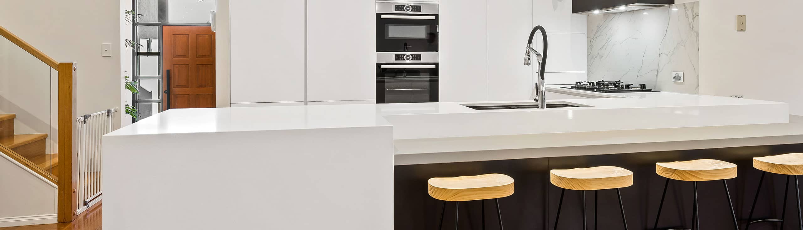 Modern white kitchen with waterfall island and timber bar stools, joinery design by Weston Kitchens