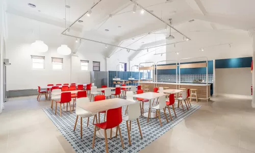 Spacious dining area with red and white chairs, tiled rug design, and modern open kitchen in back.