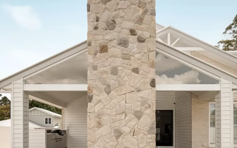 Stone chimney divides covered patio with BBQ kitchen