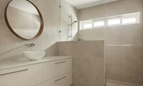 Tiled bathroom with round mirror and open shower