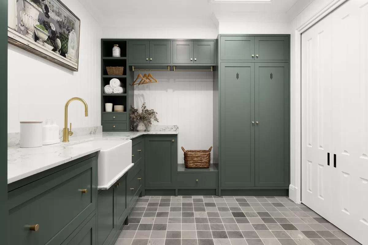 Laundry room with dark green cabinets, a white sink, gold faucet, and tiled floor.