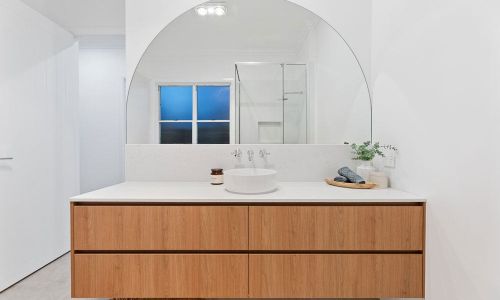 bathroom sink with wooden cabinet and half circle mirror
