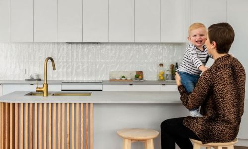 Girl sitting in a wooden high chair holding a kid on the kitchen table