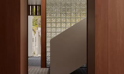 View through a wood-framed arched doorway to a staircase with a glass block wall.