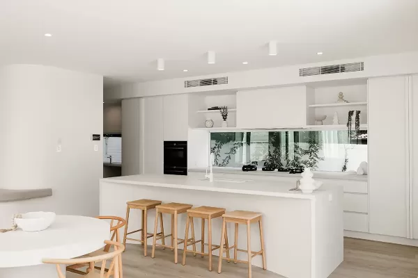 A modern kitchen with white walls and cabinets, a round dining table with wooden chairs, and a kitchen island with bar stools