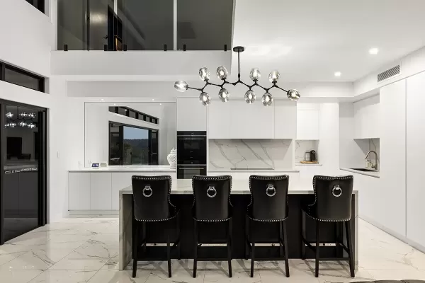 Modern kitchen interior with white cabinets, marble backsplash, and island with black high-back chairs