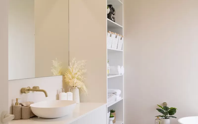 A modern bathroom with a white vanity with a single oval sink, gold faucet, and decorative dried flowers