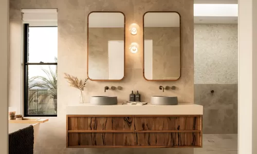 Modern bathroom with double sinks, wooden vanity, dual mirrors, wall lights, and a window with natural light