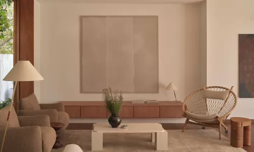 Contemporary living room in neutral tones with modern art, curved sofa, and a woven armchair.