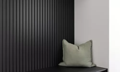 A modern mudroom with dark wood cabinetry, a black slatted wall, and a soft green cushion on the bench