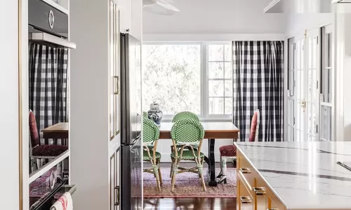 Kitchen with yellow island, marble countertop, and view into dining area with green chairs and windows