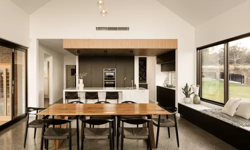 Open-plan kitchen and dining area with wooden table, modern black chairs, and large windows overlooking yard