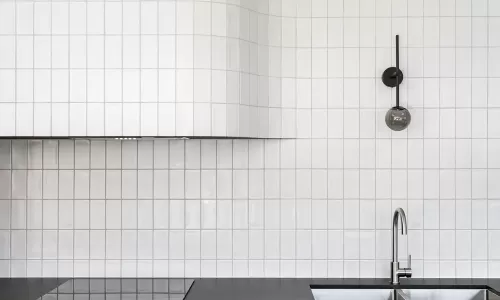 Modern kitchen with white square tile backsplash, curved hood, black cabinetry, and a sleek chrome faucet