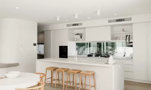 A modern kitchen with white walls and cabinets, a round dining table with wooden chairs, and a kitchen island with bar stools