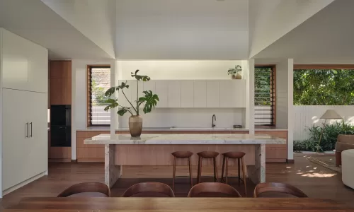 Modern kitchen and dining area with a stone island, white cabinets, and wood accents under a vaulted ceiling.