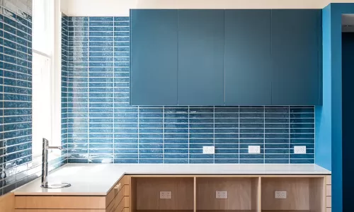 Modern kitchenette with glossy blue tile backsplash, sleek upper cabinets, and open wood shelving below.