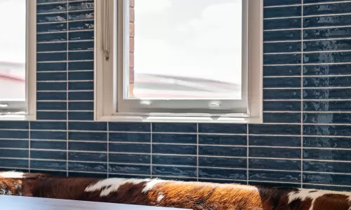 Close-up of a window-side booth with brown leather seating, cowhide cushion, and glossy blue tile wall.