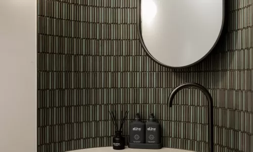 Modern powder room with curved tiled wall, floating vanity, black faucet, and oval mirror.