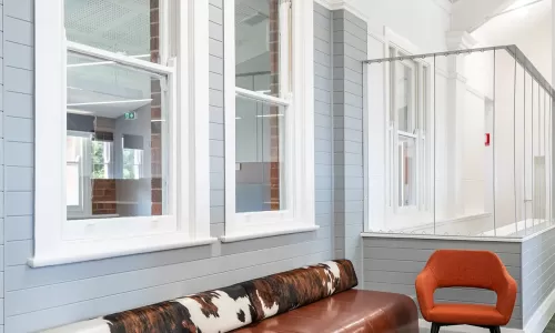 Stylish lounge with a brown leather bench, cowhide bolster, orange accent chair, and round coffee table.
