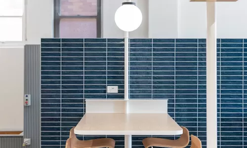 Compact high table with four wooden barstools and built-in globe light, set against dark blue tile wall.