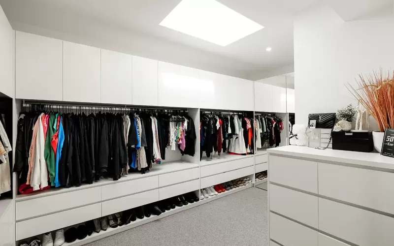 Spacious and modern walk-in closet with white cabinets, drawers, and shelves filled with clothes and shoes