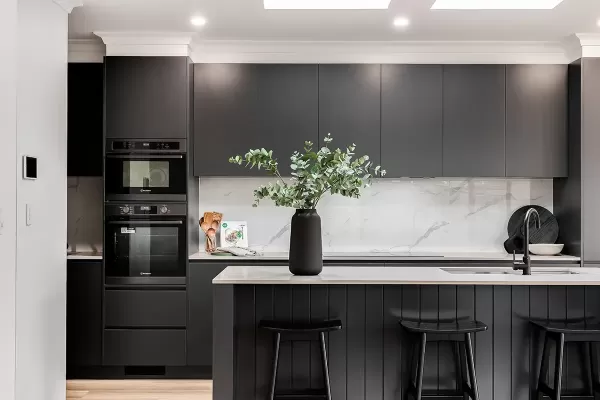 A modern kitchen with dark cabinets, white marble backsplash, and black bar stools