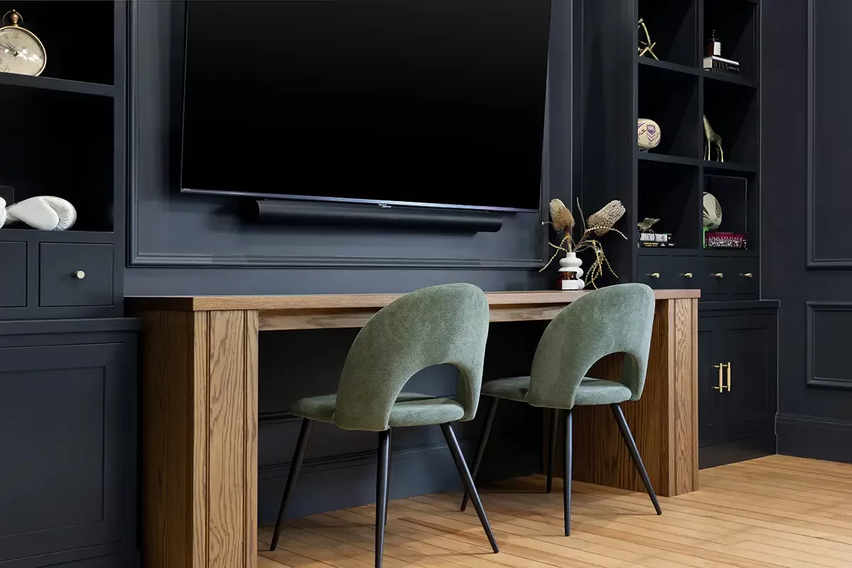 Wood desk with two green chairs under mounted TV.
