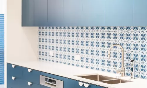 Sleek kitchen with blue cabinets, white countertop, double sink, and patterned blue-and-white backsplash.