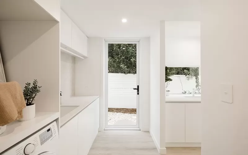 Modern minimalist laundry room with white cabinets, washing machine, and a glass door leading to the outside