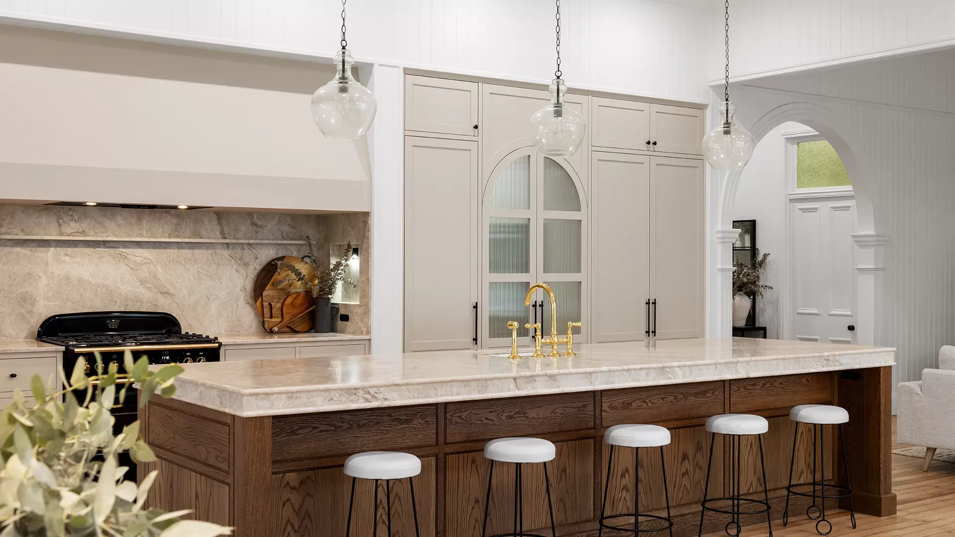 Dark wooden kitchen island with white countertop, gold faucet, and five white bar stools.