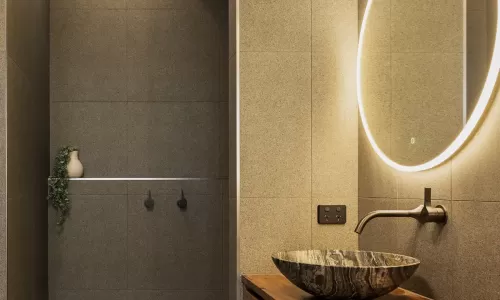 A modern bathroom with grey tiled walls, and a large round mirror with LED lighting