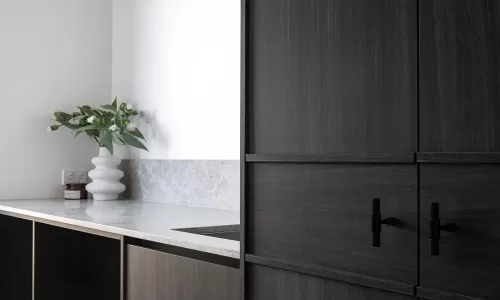 A modern laundry room with dark wood cabinetry, a marble countertop, a black hanging rod, and a white vase with greenery
