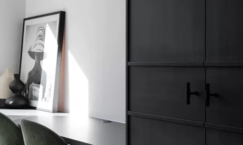 A modern home office with dark wood cabinetry, a sleek black desk, green upholstered chairs, and framed art