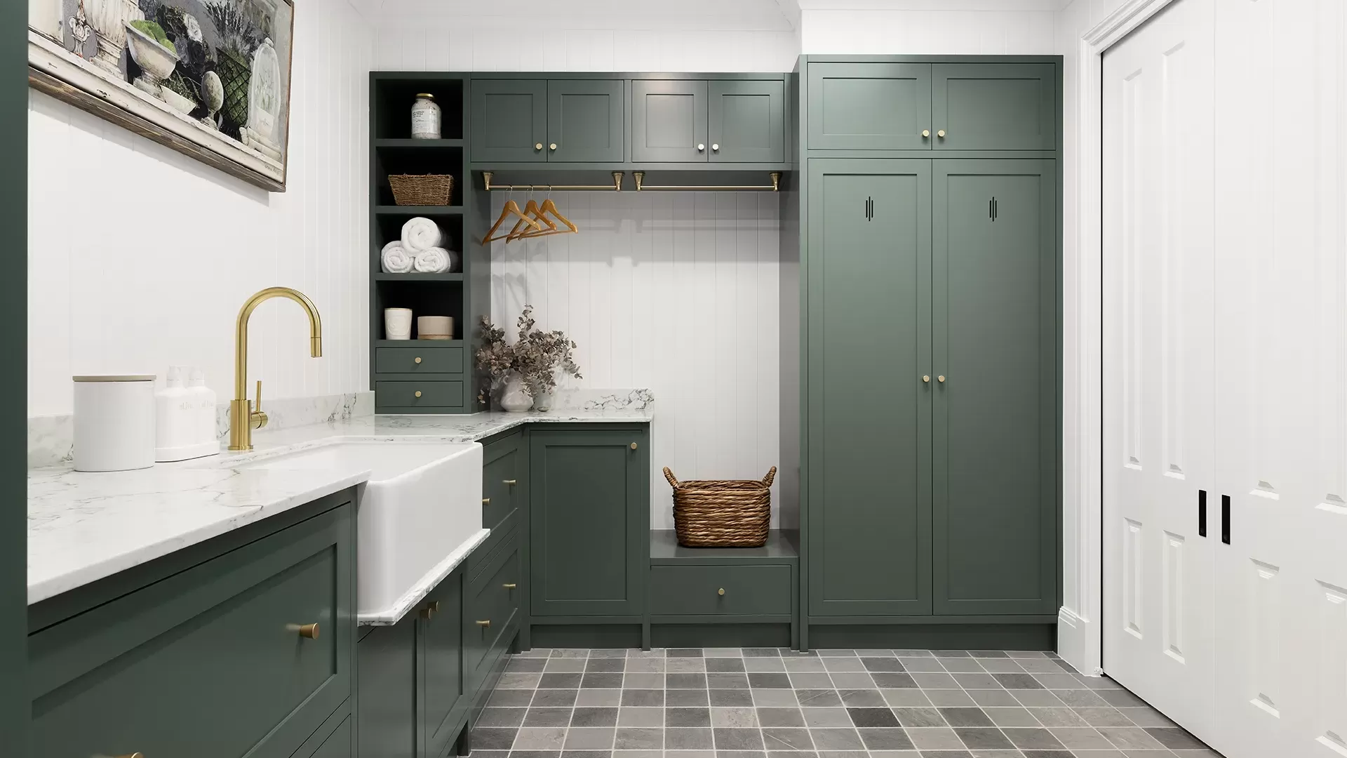 Laundry room with dark green cabinets, a white sink, gold faucet, and tiled floor.