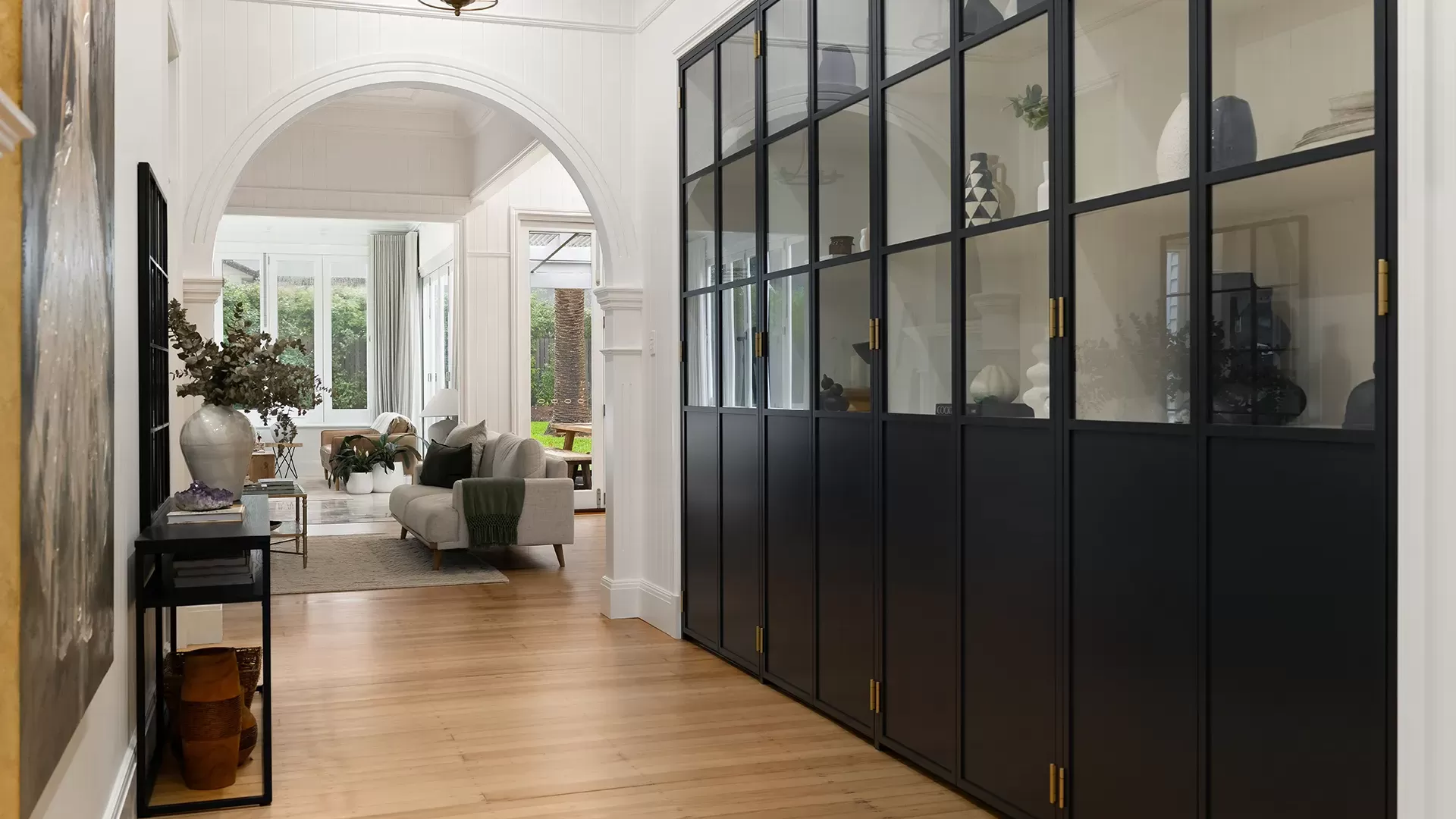 Foyer with black framed glass cabinet doors, a large archway, and wood floors.