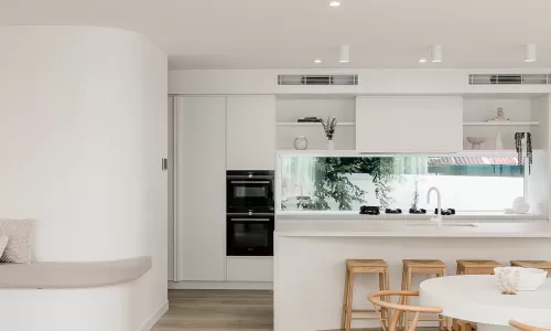 A modern kitchen with white walls, wooden flooring, and a built-in oven