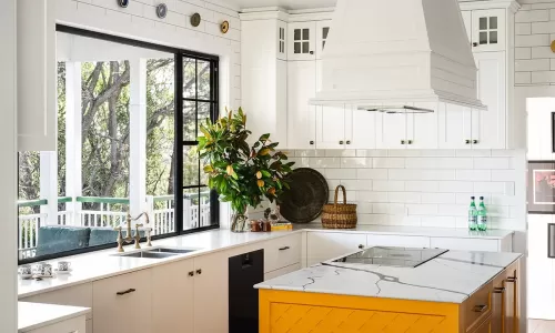 Modern kitchen with white cabinets, large window, yellow island, marble countertop, and green plant