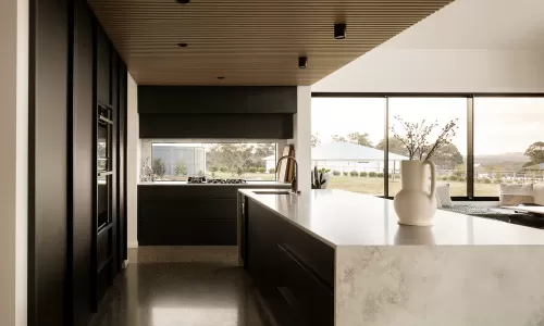 Modern kitchen with black cabinetry, marble countertops, and large windows offering a scenic outdoor view