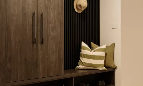 Mudroom with dark wood storage, cushioned bench, striped pillow, and organized shoe shelves.
