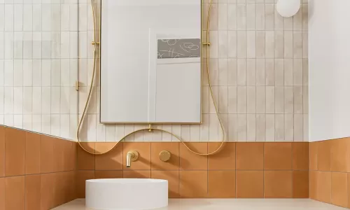 A modern bathroom with a gold-framed mirror, and white and brown tiles