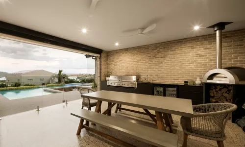Outdoor kitchen with brick wall, barbecue grill, wood-fired oven, dining table, and pool view