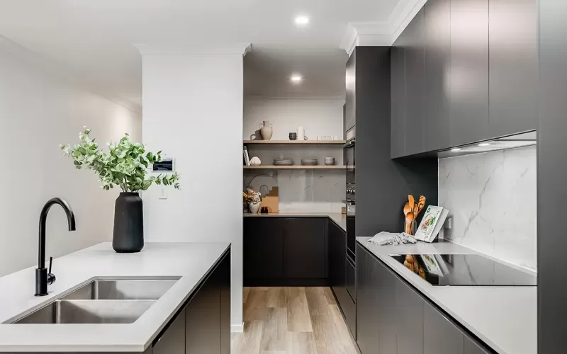Modern kitchen with dark gray cabinets, white marble backsplash, stainless steel sink and faucet, and wooden flooring