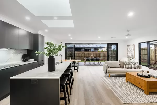 A modern open concept kitchen and living area with large windows, dark cabinetry, a kitchen island with bar stools, a dining table, and a cozy sitting area